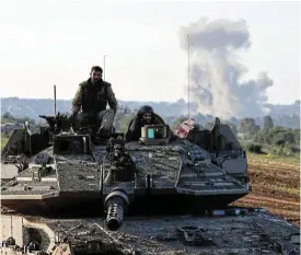  ?? /Reuters ?? Military might: Smoke rises in the distance as Israeli soldiers ride a tank. Israel’s military says it will devote months of more targeted operations against leaders and positions of Hamas.