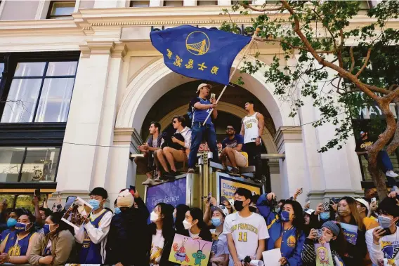  ?? Marlena Sloss / Special to The Chronicle ?? Takuya Miwa of San Mateo waves a Golden State Warriors flag with Chinese lettering before the team’s championsh­ip parade in downtown San Francisco.