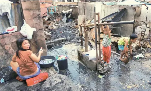  ??  ?? A survivor washes the family’s laundry, while her son helps her at the water pump and another child gathers some debris. Some of the families have chosen to return to their home lots, instead of staying in two gyms set aside for fire victims.