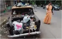  ??  ?? An Indian woman speaks on her mobile phone while walking past a Premiere Padmini taxi used as a garbage vat in Mumbai.