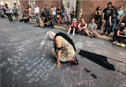  ??  ?? Lise Stoessel, from Charlottes­ville, writes a message on Sunday at a memorial at the site of a deadly car attack there a day earlier. PICTURE: EVELYN HOCKSTEIN FOR THE WASHINGTON POST