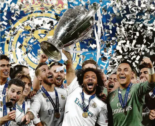  ?? Lluis GENE/AFP ?? O lateral esquerdo Marcelo ergue o troféu da Liga dos Campeões da Europa, o seu quarto pelo Real Madrid; após muita festa pela conquista do título, ele e Casemiro, além de Roberto Firmino, do Liverpool, se apresentam amanhã ao técnico Tite, na Inglaterra