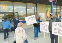  ?? TED SLOWIK/DAILY SOUTHTOWN ?? Mayor Joseph Roudez holds a door Tuesday as residents pass signs held by Mildred Morgan and Gregory Box.