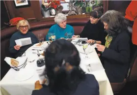  ?? Scott Strazzante / The Chronicle ?? Barbara Blake (left), Leonie Van Den Berg, volunteer Kim Rotchy and Kathleen McClay read a newspaper article at Fior d’Italia in San Francisco during a Dec. 18 book club meeting organized by NEXT Village SF.