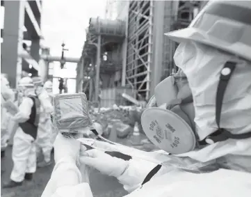  ??  ?? A worker measures the radiation in the air as employees in protective clothing prepare materials used to create a frozen undergroun­d wall to surround the crippled reactor buildings at Tokyo Electric Power Co.’s Fukushima Dai-ichi nuclear power plant in...