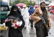  ?? EBRAHIM NOROOZI / AP ?? An Afghan woman walks through the old market as a Taliban fighter stands guard, in downtown Kabul, Afghanista­n, on Tuesday.