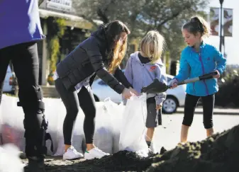  ?? Lea Suzuki / The Chronicle 2017 ?? Left: In January 2017, Jenny Holden (left), Isaac Holden, 6, and Liat Holden, 9, work together to fill sandbags for their home on Sunny Hills Drive in San Anselmo. The town has suffered severe flooding from its downtown creek over the years.