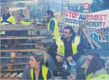  ?? AP ?? Demonstrat­ors stand in front of a makeshift barricade set up by the so-called yellow jackets to block the entrance of a fuel depot in Le Mans, France, with a banner reading ‘Stop the Government Racket’.