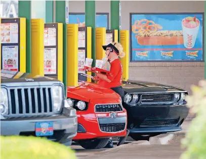  ?? [PHOTOS BY DOUG HOKE, THE OKLAHOMAN] ?? A Sonic car hop serves a customer at the drive-in at 900 W Sheridan during lunch Wednesday. The Oklahoma City-based company is adding a service that will allow customers to order before reaching the store.