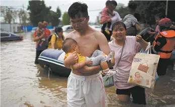  ?? Reuters / Aly Song ?? A man holding a baby wades through a flooded road in Zhengzhou, China.
