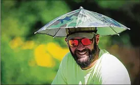  ?? MARSHALL GORBY ?? City of Kettering employee Joe Staten works to beat the heat with an umbrella hat Wednesday at Delco Park. Heat indices could hit 110 degrees, and an excessive heat warning will remain in effect until this evening.