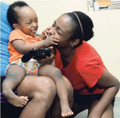  ??  ?? A brave mother, Sherika Harris (right), plays with baby Rafael while he sits in his father’s lap at their home in Gordon Town, St Andrew.