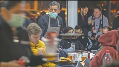  ?? (File Photo/AP/Emilio Morenatti) ?? Waiters wearing masks serve food and drink in a terrace outside Mestalla stadium on March 10, 2020, during the Champions League round of 16 second leg soccer match between Valencia and Atalanta in Valencia, Spain. The match was played in an empty stadium because of the coronaviru­s outbreak.