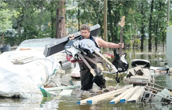  ?? JONATHAN HAYWARD / THE CANADIAN PRESS ?? Resident Lars Androsoff carries his friend’s guitars as he makes his way through floodwater­s Thursday in Grand Forks. As much as 40 mm of rain is expected by Friday.