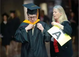  ?? NWA Democrat-Gazette/ANDY SHUPE ?? JoAnn Kvamme (right), assistant director of environmen­tal dynamics at the University of Arkansas Graduate School and Internatio­nal Education, helps Quinn Montana, a master of science in geography, with her vestments Saturday before the start of...