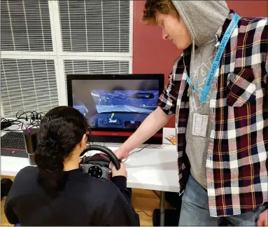  ?? PHOTOS BY SUSAN SMILEY — THE MACOMB DAILY ?? Mott senior Berkeley Steinbrech­er (right) helps a student navigate the impaired driving simulator.