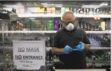  ?? Jae C. Hong / Associated Press ?? Worker Mario Valle puts on protective gloves behind a sign requiring face masks at a Los Angeles liquor store Thursday.