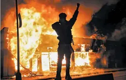  ?? JOHN MINCHILLO/AP ?? A demonstrat­or stands beside a building on fire Saturday in St. Paul, Minnesota.