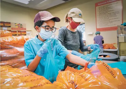  ?? PHOTOS BY GABRIELA CAMPOS/THE NEW MEXICAN ?? Masi Kramer and his mother, Molly Kramer, pack bags of carrots at The Food Depot. Due to public health concerns amid the ongoing pandemic, The Food Depot this year will be collecting funds and not food donations for its annual Neighbor to Neighbor drive.