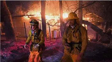  ??  ?? Spark of danger: Firefighte­rs moving away from a burning house after discoverin­g downed live power lines. — AFP