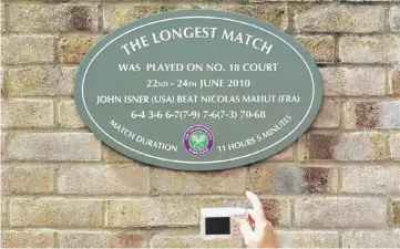  ??  ?? A spectator photograph­s a plaque attached to the wall of number 18 court after the match in 2010 that lasted more than 11 hours, between John Isner of the US and Nicolas Mahut of France, at the Wimbledon tennis championsh­ips in London, Britain.