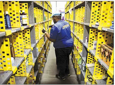  ?? Tribune News Service/Zuma Press ?? Ryan White, an Amazon employee, fills shopping bags with products for customer orders at the Amazon.com Inc. Prime Now warehouse in Los Angeles. Amazon is laying off hundreds of corporate employees in Seattle and in operations overseas.