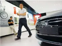  ?? AFP/Getty Images files ?? A man walks past a Tesla car at a company showroom in Beijing. Tesla is rushing to expand its network of charging stations in China to assuage range anxiety and is adding luxury features.