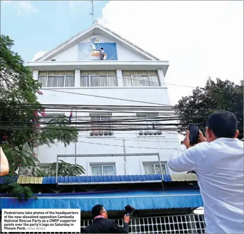  ?? HONG MENEA ?? Pedestrian­s take photos of the headquarte­rs of the now-dissolved opposition Cambodia National Rescue Party as a CNRP supporter paints over the party’s logo on Saturday in Phnom Penh.