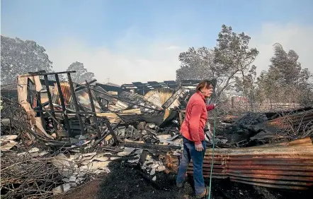  ?? FAIRFAX ?? Steff Pedersen hoses down his son’s shed at a property on the Princes Highway that was lost in a fire in Bomaderry, New South Wales.