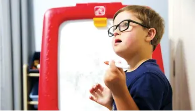  ?? STAFF PHOTO BY ERIN O. SMITH ?? Coleson Penney, 6, talks to his mom as he writes on his board Friday at his family’s home. The Penneys moved into the school zone for Westview Elementary, which has a history of including students with disabiliti­es in general education classrooms.