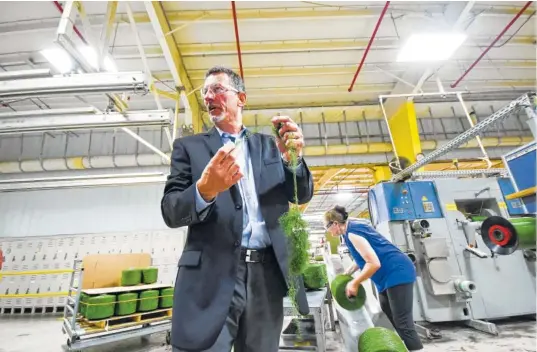  ?? STAFF PHOTOS BY TIM BARBER ?? TenCate vice president of operations Matt Stubblefie­ld holds a spool of synthetic fiber while talking about thread count. Bonnie Bacon, back right, works and pulls tails from the spools to confirm a thread count.