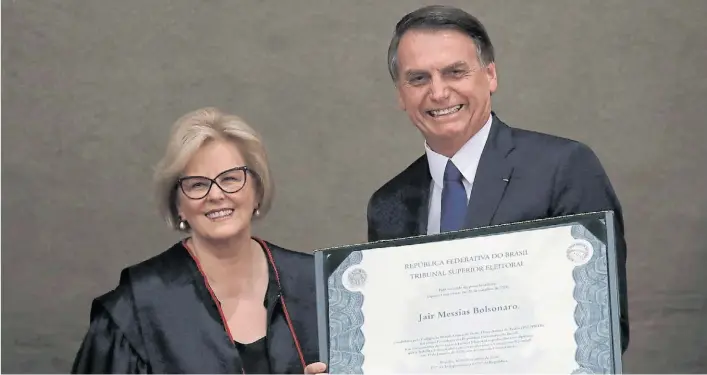  ?? BLOOMBERG ?? Diploma oficial. Jair Bolsonaro recibe de la titular del Tribunal Supremo Electoral, Rosa Weber, el certificad­o que lo acredita como presidente electo de los brasileños.