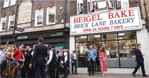  ??  ?? People watch from the windows above Beigel Bake Brick Lane Bakery as Prince William and his wife Catherine leave after visiting the bakery in east London yesterday. The 24-hour bakery was forced to reduce their opening hours during the pandemic and The Duke and Duchess heard how this affected employees, as well as the ways in which the shop has helped the local community through food donation and delivery.