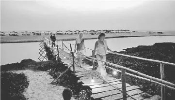  ?? — AFP photo ?? This file photo shows western tourists walking along a wooden bridge at dusk at Mandrem Beach in the Indian state of Goa.