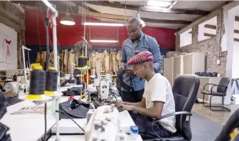  ?? ?? Tshepo Mohlala (left), founder of Tshepo Jeans, looks at a sewer’s work in his workshop in Johannesbu­rg.