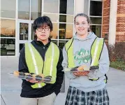  ?? [PHOTO PROVIDED] ?? Bishop McGuinness Catholic High School students Nayos Sirisoot and Olivia Schmidt were ready to hand out muffins to parents in the car pool line during Catholic Schools Week.