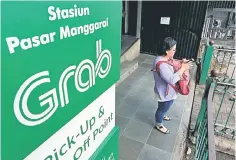  ??  ?? A woman uses her phone near a sign for the online ride-hailing service Grab at the Manggarai train station in Jakarta. Indonesia has set minimum and maximum tariffs for online car-hailing services, aiming to ensure comparable pricing with convention­al...