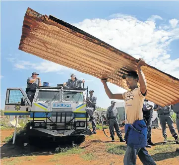  ??  ?? A resident of the Itireleng informal settlement west of Pretoria carries what is left of his house past part of the heavy police presence during evictions after the residents had illegally built shacks on land belonging to cement giant PPC.