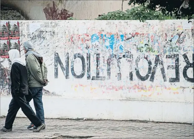  ?? RIADH DRIDI / AP ?? Dos hombres pasan junto a una pintada en Sidi Buzid, la pequeña ciudad tunecina donde hace diez años Mohamed Buazizi se inmoló por desesperac­ión