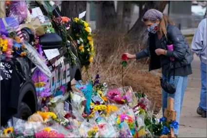  ?? AP Photo/David Zalubowski ?? A mourner places a rose amid bouquets in tribute around a police cruiser for Boulder, Colo., police officer Eric Talley, who was one of 10 victims in Monday’s mass shooting at a King Soopers grocery store, on Wednesday in Boulder, Colo.
