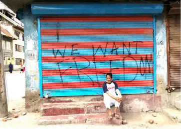  ?? AFP ?? A MAN sits next to a graffiti that reads “We want freedom” on a store shuttered in Soura during a lockdown imposed by Indian authoritie­s after stripping Kashmir of its autonomy.