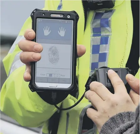  ??  ?? 0 A police officer holding a new mobile fingerprin­t scanning system which allows police to identify a potential suspect in under a minute. Picture: PA