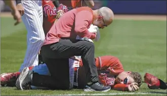  ?? AP photo ?? A trainer checks on Phillies first baseman Rhys Hoskins after he was injured fielding a grounder during a spring training game Thursday.