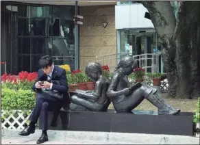  ?? PHOTO BY EDMOND TANG ?? An office worker sits glued to his smartphone next to a bronze statue of two children reading books outside Hong Kong’s Central Library in Causeway Bay. Seeing people engrossed in their phones is an everyday phenomenon on Hong Kong streets.