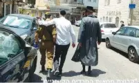  ?? (Extremist Protest Group) ?? A TOLDOT AHARON Hassid (right) and another haredi man escort a soldier away from an anti-Zionist mob in the capital’s Mea She’arim neighborho­od on Friday.