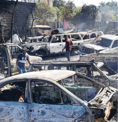  ?? ?? Inwoners van Haïti zoeken maandag in de hoofdstad Port-au-Prince naar bruikbare onderdelen van uitgebrand­e auto’s, bij een garage die tijdens de recente geweldsgol­f in het land in brand werd gezet door gewapende bendes.