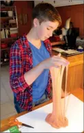  ?? The Associated Press ?? Astrid Rubens demonstrat­es the elasticity of homemade slime in her kitchen in St. Paul, Minn. Glue, baking soda and contact lens solution are all it takes to make satisfying­ly stretchy slime.