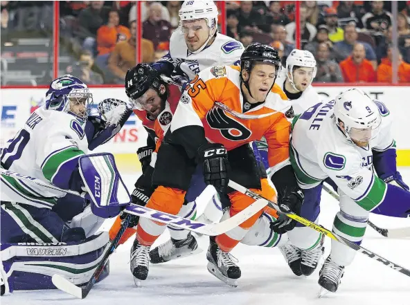  ?? — GETTY IMAGES ?? Flyers forward Nick Cousins is checked by Canucks defenceman Nikita Tryamkin, centre, near Vancouver’s net during the Flyers’ 5-4 shootout win Thursday night in Philadelph­ia. Claude Giroux was the only player to score in the penalty shot duel.