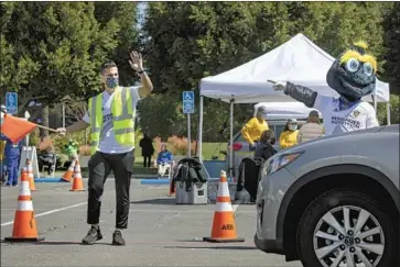  ?? Myung J. Chun Los Angeles Times ?? GALAXY MIDFIELDER Sebastian Lletget and team mascot Cozmo direct traffic at Dignity Health Sports Park in Carson during a COVID-19 vaccinatio­n drive Tuesday. More than 4,000 cars came in one day.