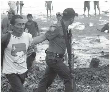  ?? JUDY FLORES PARTLOW ?? A policeman arrests one of two men during the commotion at the barricade in protest of " black sand mining" at the dredging project site in Tambacan, Tanjay City.